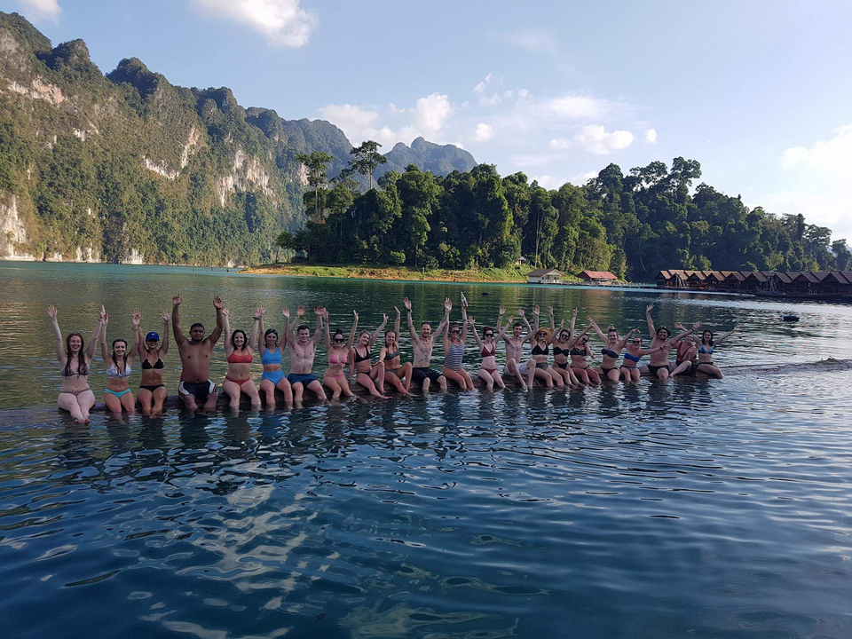 A group of people on a log posing in a lake.
