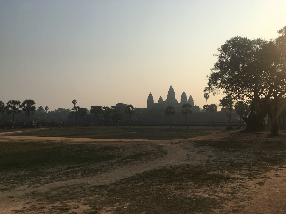 View of Angkor Wat in silhouette at sunset with surrounding trees.