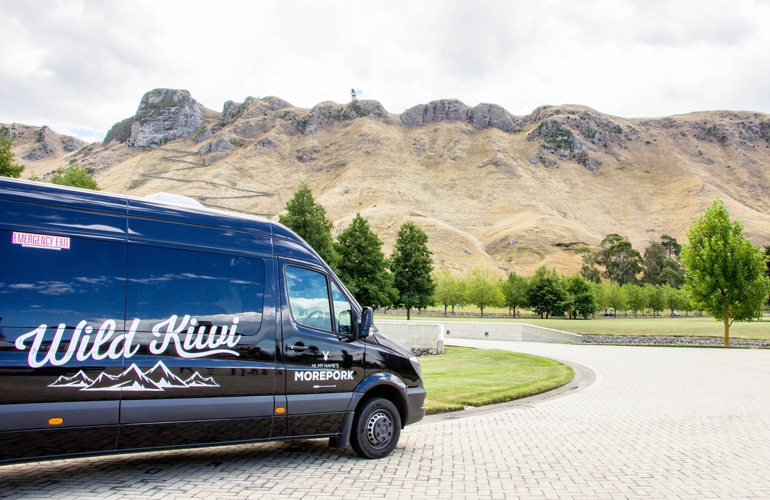 Fourgon nommé Wild Kiwi stationné avec des montagnes en arrière-plan.