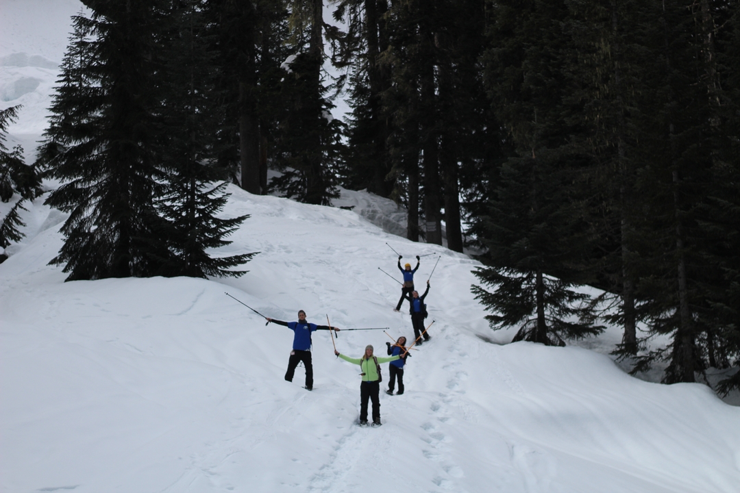 Quatre personnes posant dans la neige, écartant les bras et les bâtons.