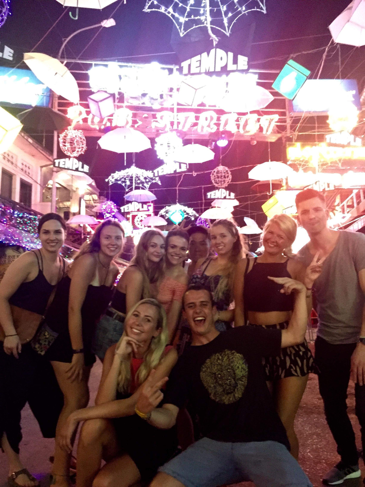 Amis posant sous des parapluies colorés dans un marché de nuit.