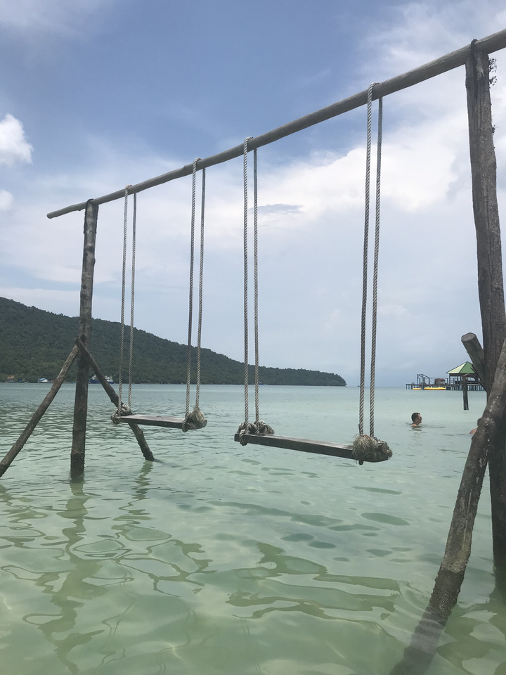 Wooden swings in the sea with a person swimming nearby.