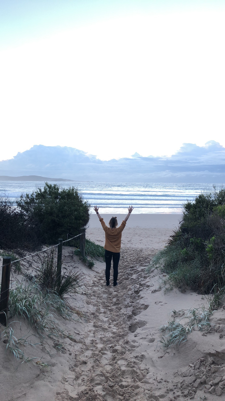 A person with arms raised facing the ocean at dusk.