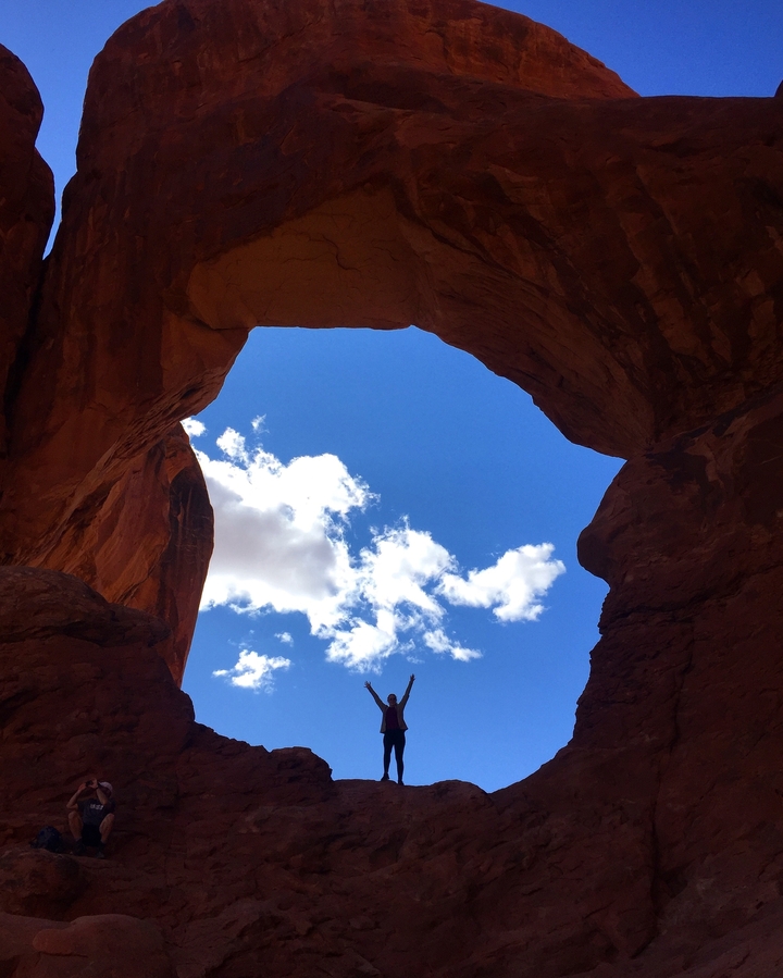 Personne avec les bras levés sous une arche rocheuse naturelle.