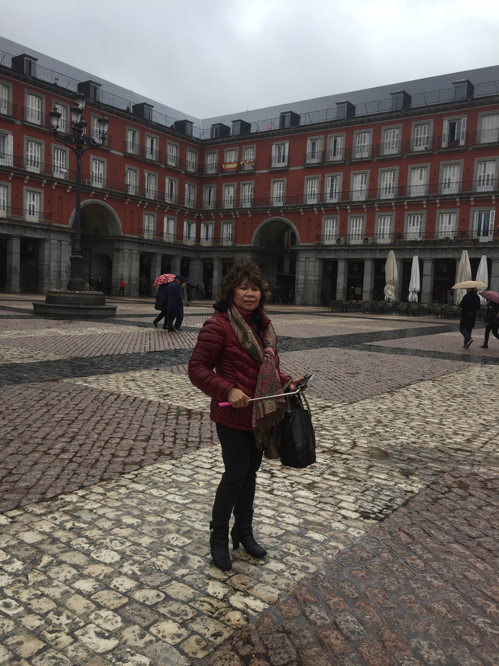 Une personne debout avec un parapluie sur une place avec des bâtiments historiques.