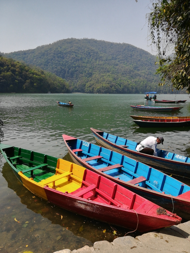 Bateaux colorés sur un lac calme avec des collines brumeuses en arrière-plan.