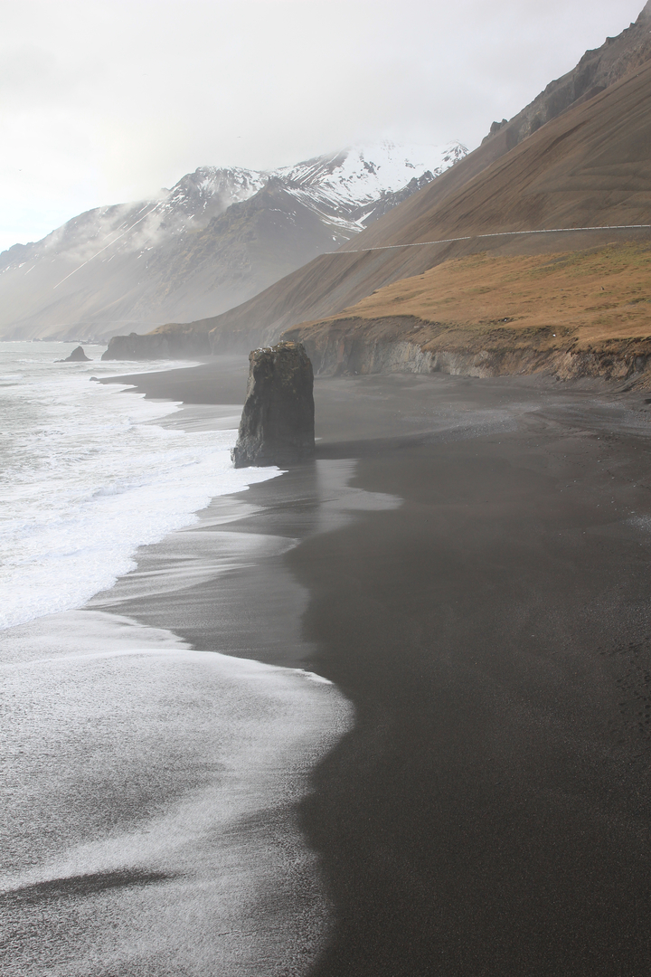 Black sand beach with large rock formations.