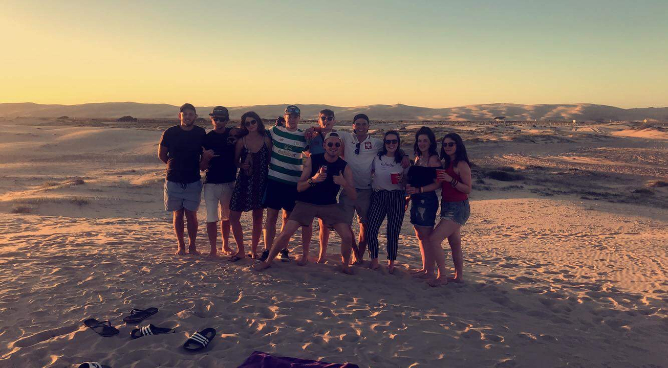 Group photo of friends at the beach during sunset.