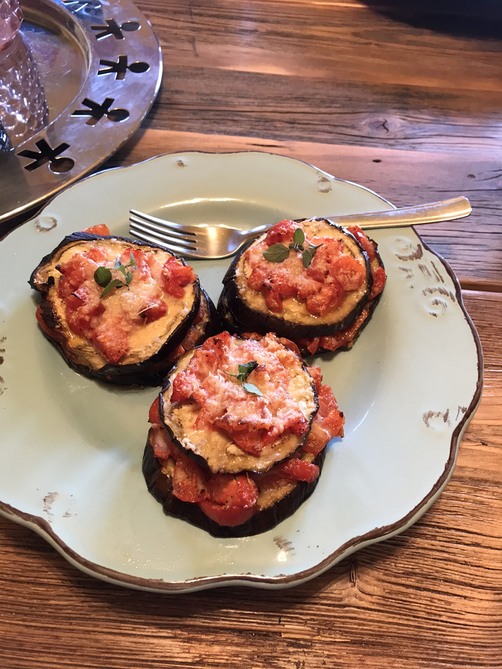 Plat composé d'aubergines cuites au four, garnies de tomates et de fromage.