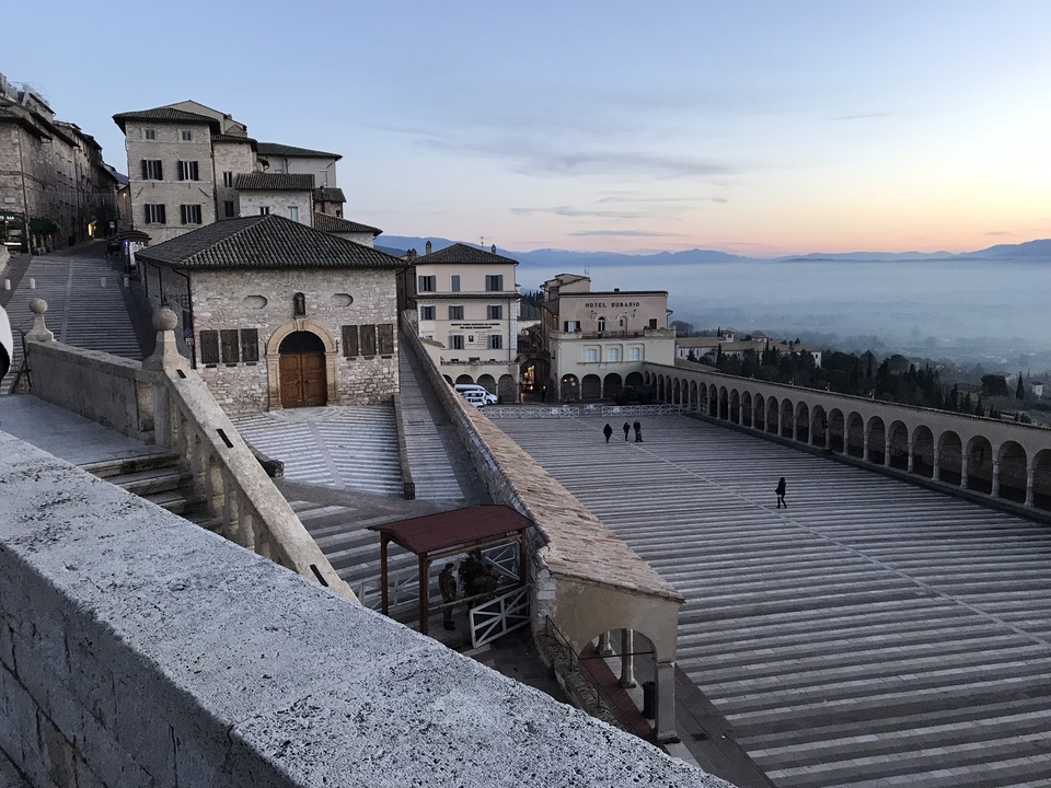 Vue de la terrasse d'Assise avec coucher de soleil et brume.