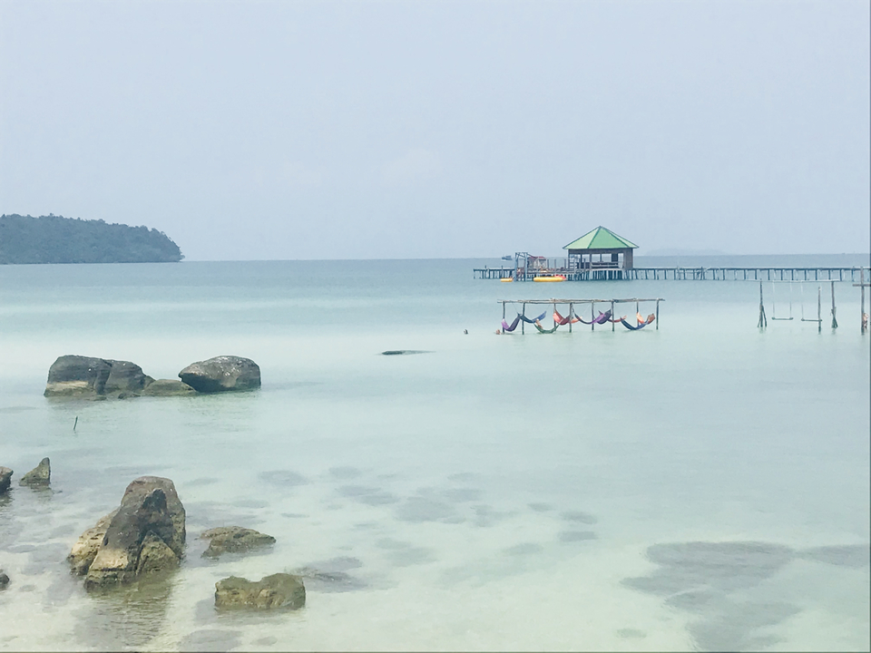 Beach with hammocks over crystal clear water, scenic backdrop.