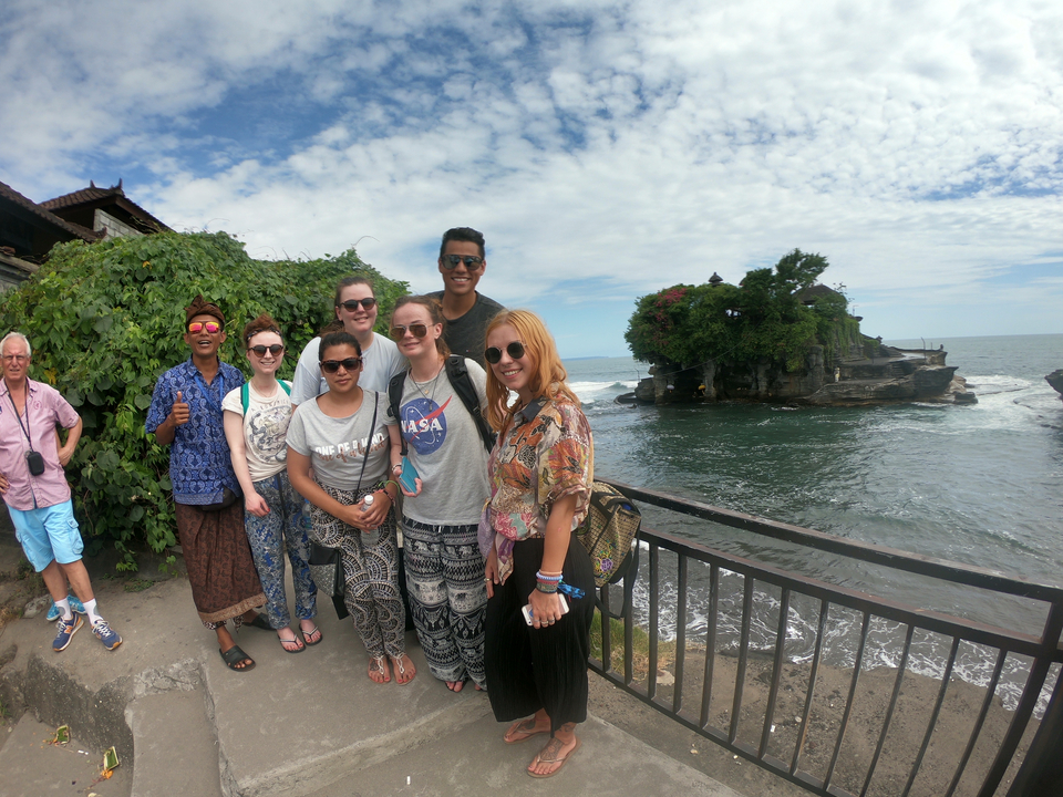 Group of people posing by the sea with a landmark in the background.