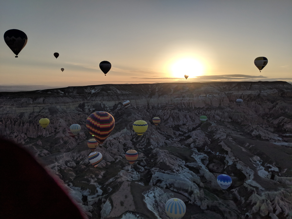 Montgolfières flottant au lever du soleil sur un terrain rocailleux.