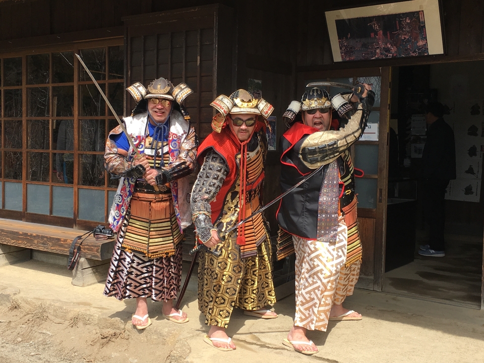 Trois personnes vêtues de costumes de samouraïs prennent des poses énergiques.