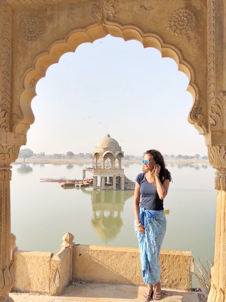 Une femme portant des lunettes de soleil se tient dans un pavillon surplombant un lac avec des bateaux.