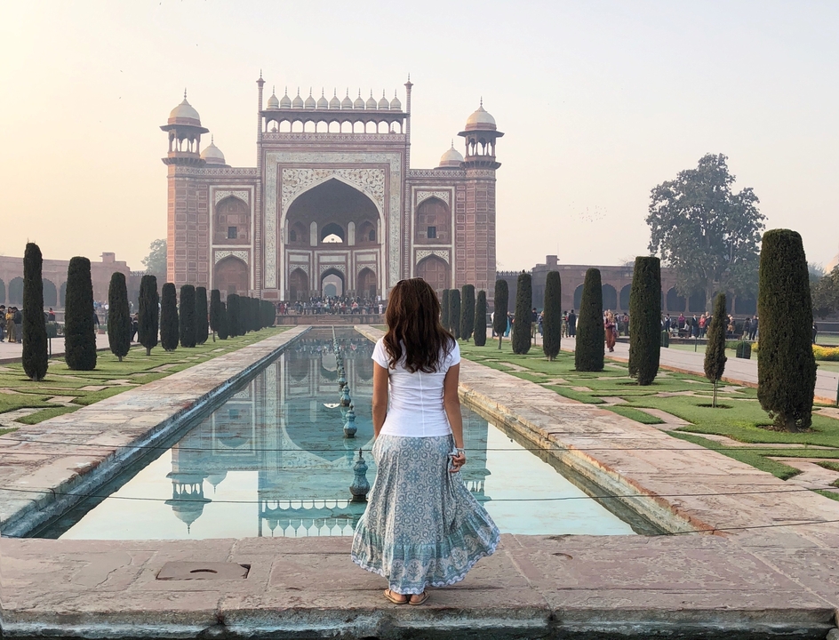 Une femme se tient près d'un bassin réfléchissant menant à une porte ornée à l'architecture moghole.