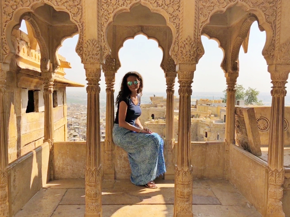 Une femme est assise dans un pavillon aux arches sculptées surplombant un paysage désertique.