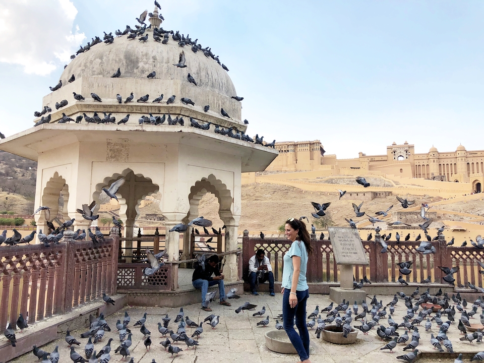 Une femme se tient au milieu de pigeons près d'un fort historique.
