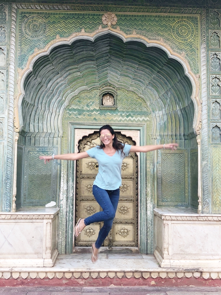 Une femme en jean et t-shirt pose joyeusement devant une porte décorative.