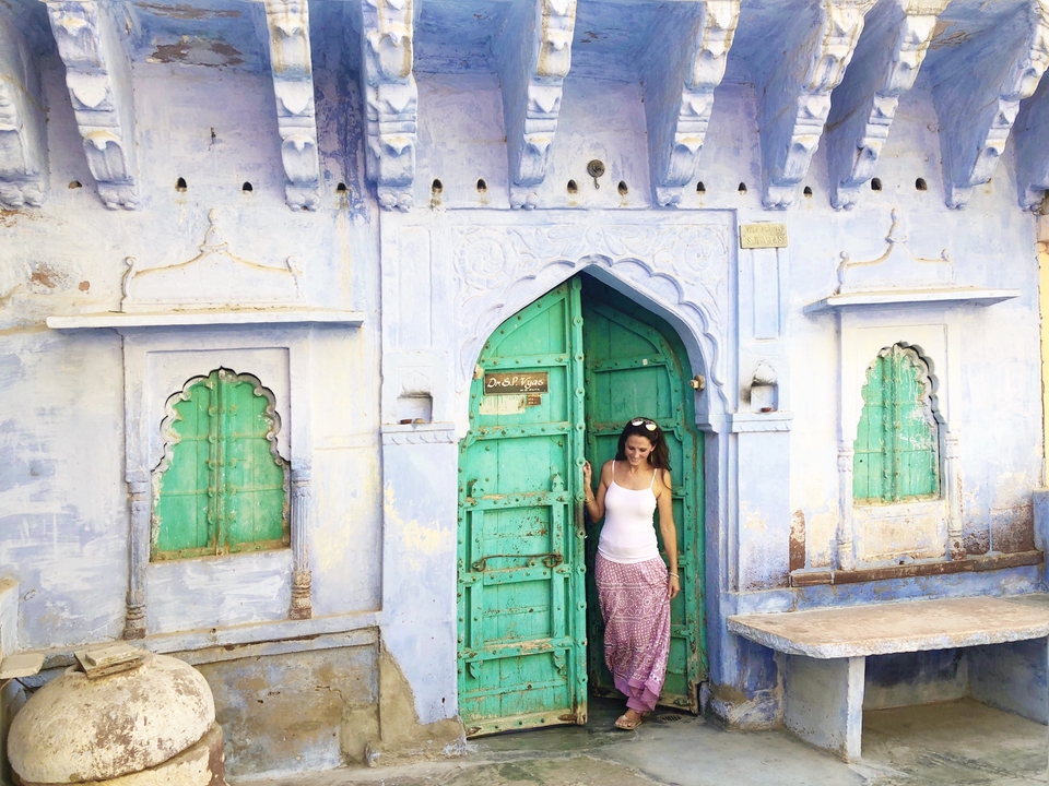 Une femme se tient dans l'embrasure d'un bâtiment bleu aux motifs complexes.