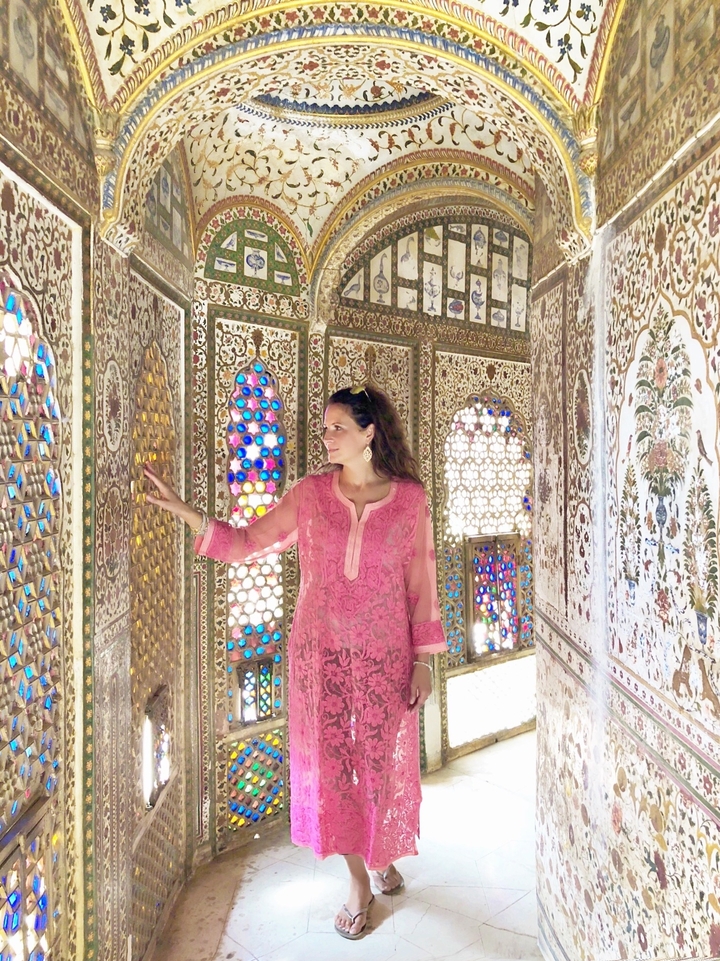 Une femme en tenue traditionnelle rose touche un mur décoré.