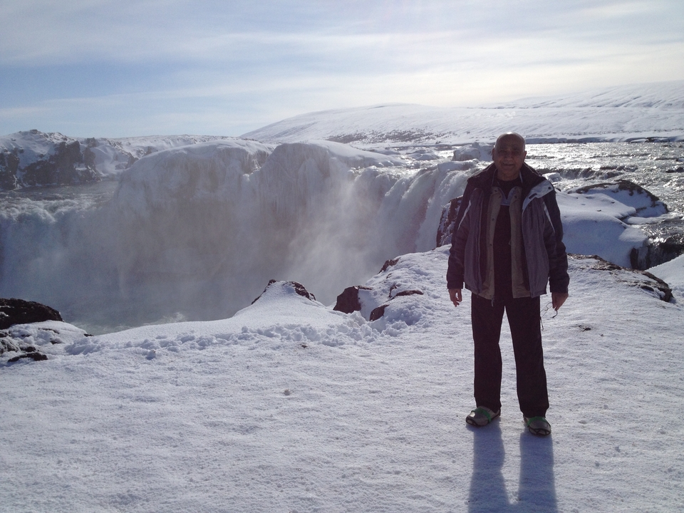 Personne debout devant une chute d'eau enneigée.