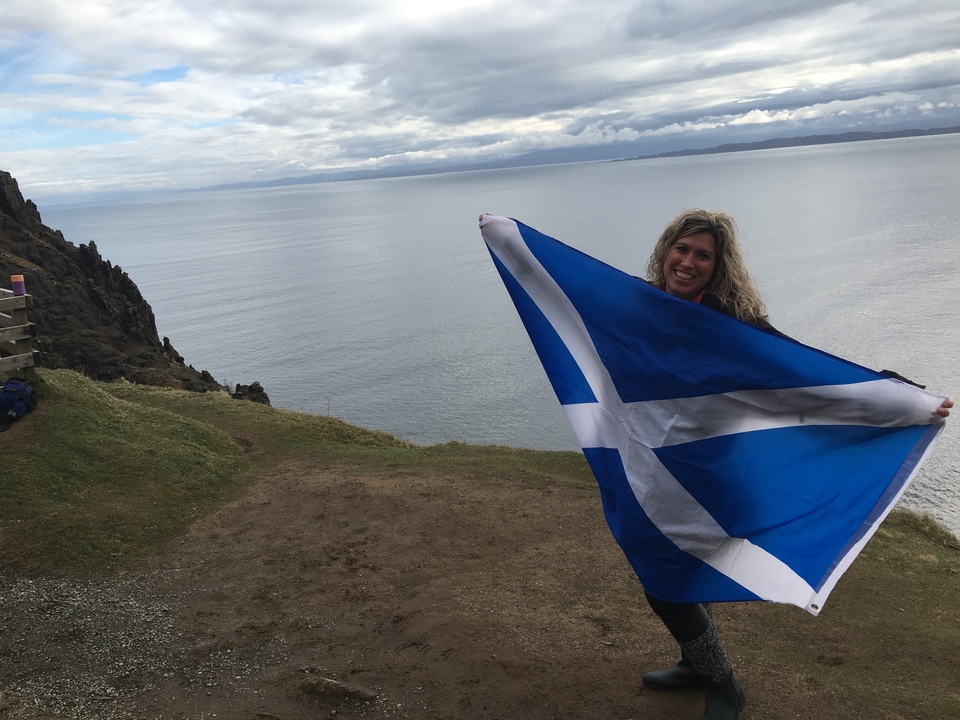 Woman holding a Scottish flag on a cliffside.