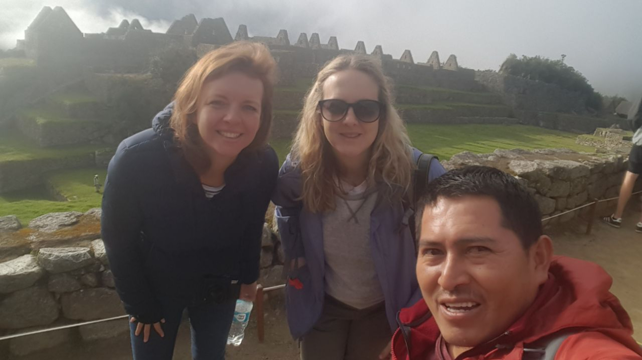 Touristes prenant un selfie devant d'anciennes ruines avec des terrasses en pierre.