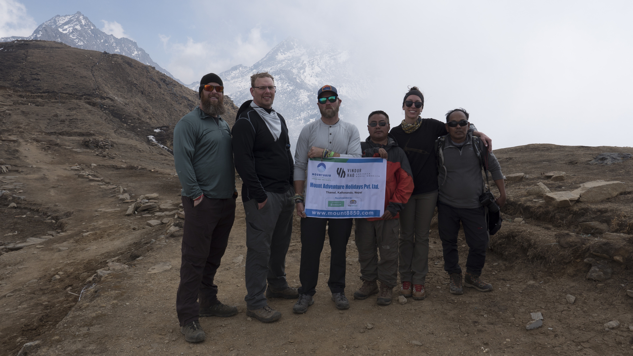 Groupe de personnes posant avec un drapeau dans une zone montagneuse.