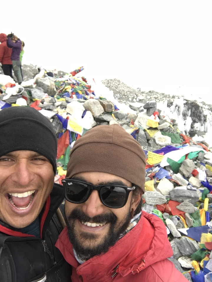 Deux personnes souriant devant des drapeaux de prière et des cairns.