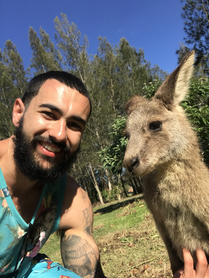 Person smiling next to a kangaroo in a natural setting.