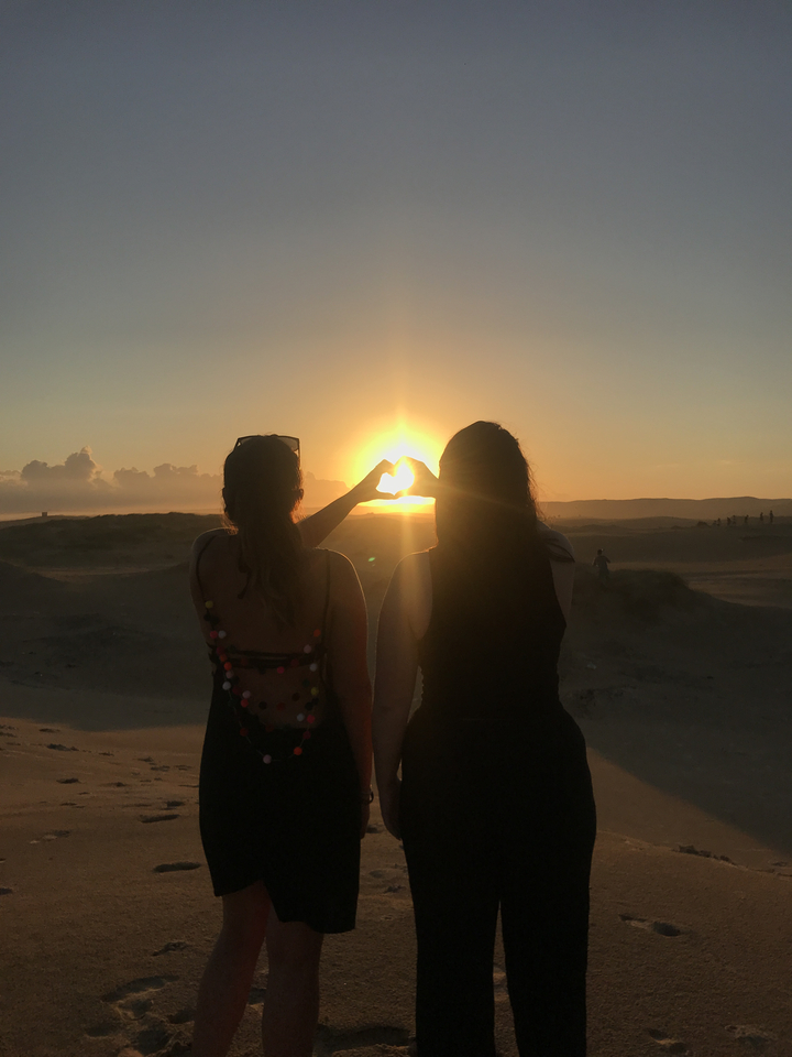 Silhouette of two people forming a heart shape with their hands at sunset.