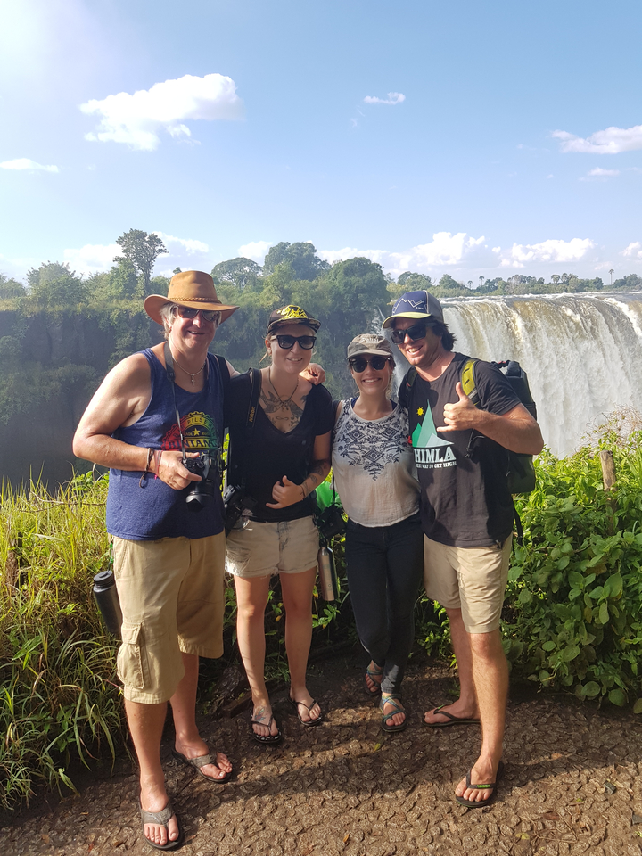 A group of tourists posing with Victoria Falls in the background.