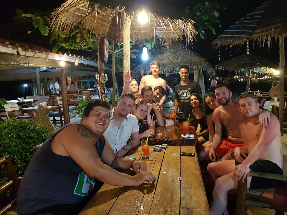 A group of people sitting around a large wooden table at a nighttime gathering.