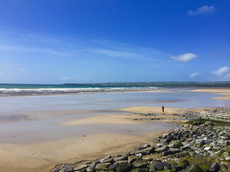 Vue panoramique d'une plage avec une personne seule en train de marcher.