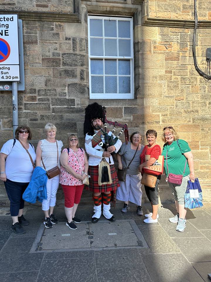 Groupe de touristes avec un joueur de cornemuse dans une rue pavée.