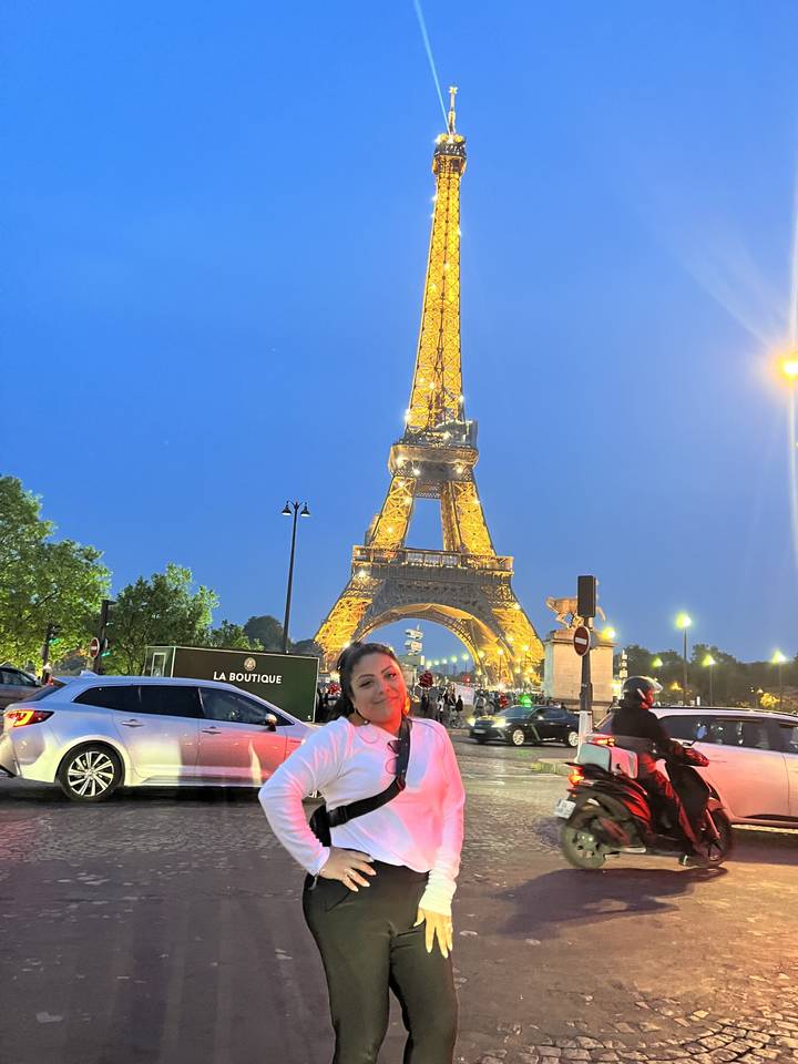 Person posing in front of the illuminated Eiffel Tower at night.