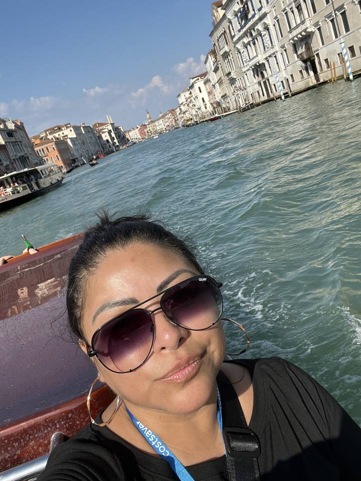 Person in sunglasses on a boat with Venice in the background.