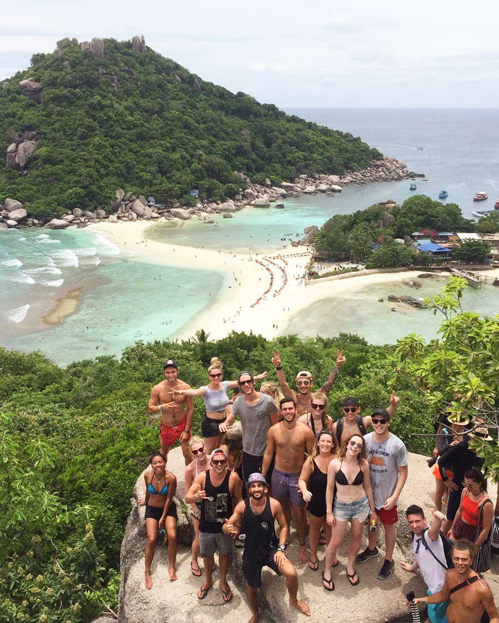 A large group of people posing on a viewpoint overlooking a beach.
