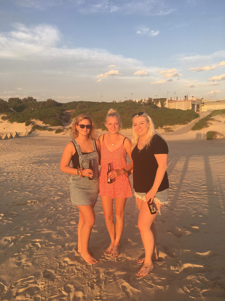 Three friends holding drinks on the beach at sunset.