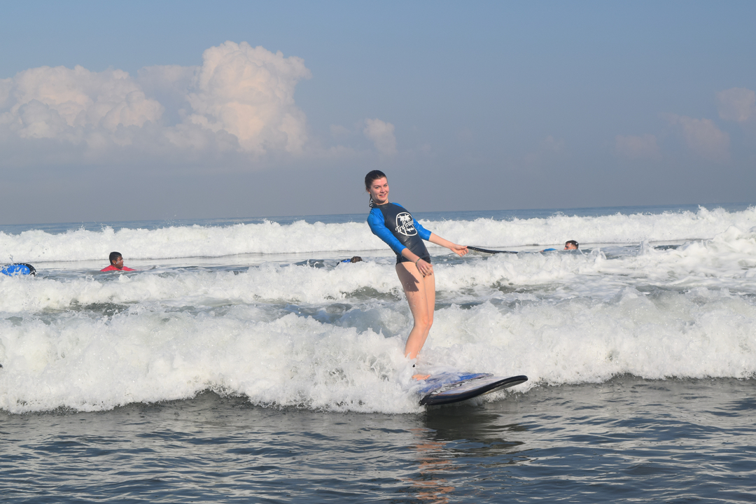 Woman surfing on a wave with others visible in the background.
