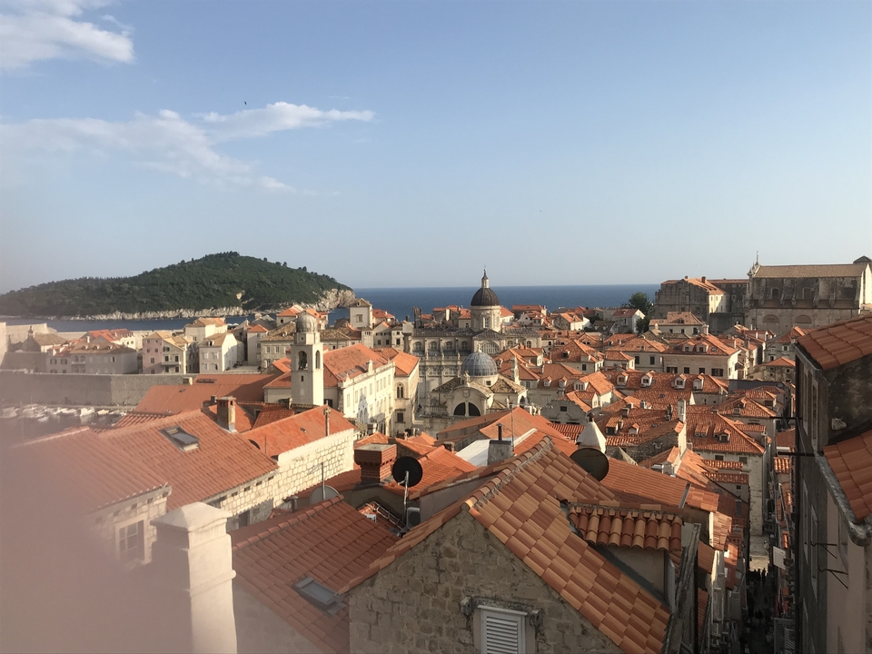 Vue panoramique d'une ville historique aux toits de terre cuite et d'une île lointaine.