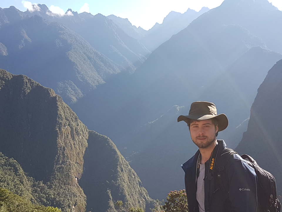 Voyageur avec un chapeau posant devant un arrière-plan montagneux avec un éclairage dramatique.