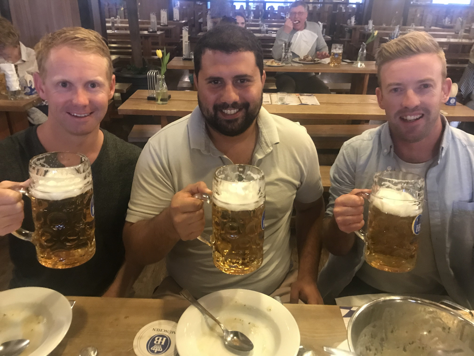 Trois hommes tenant de grandes chopes de bière à une table à l'intérieur d'une brasserie.
