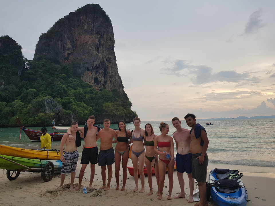Group of people posing on a beach with a cliff.