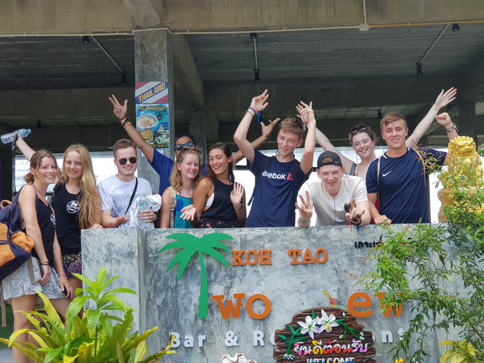 Group of people smiling and cheering with a 'Koh Tao' sign.
