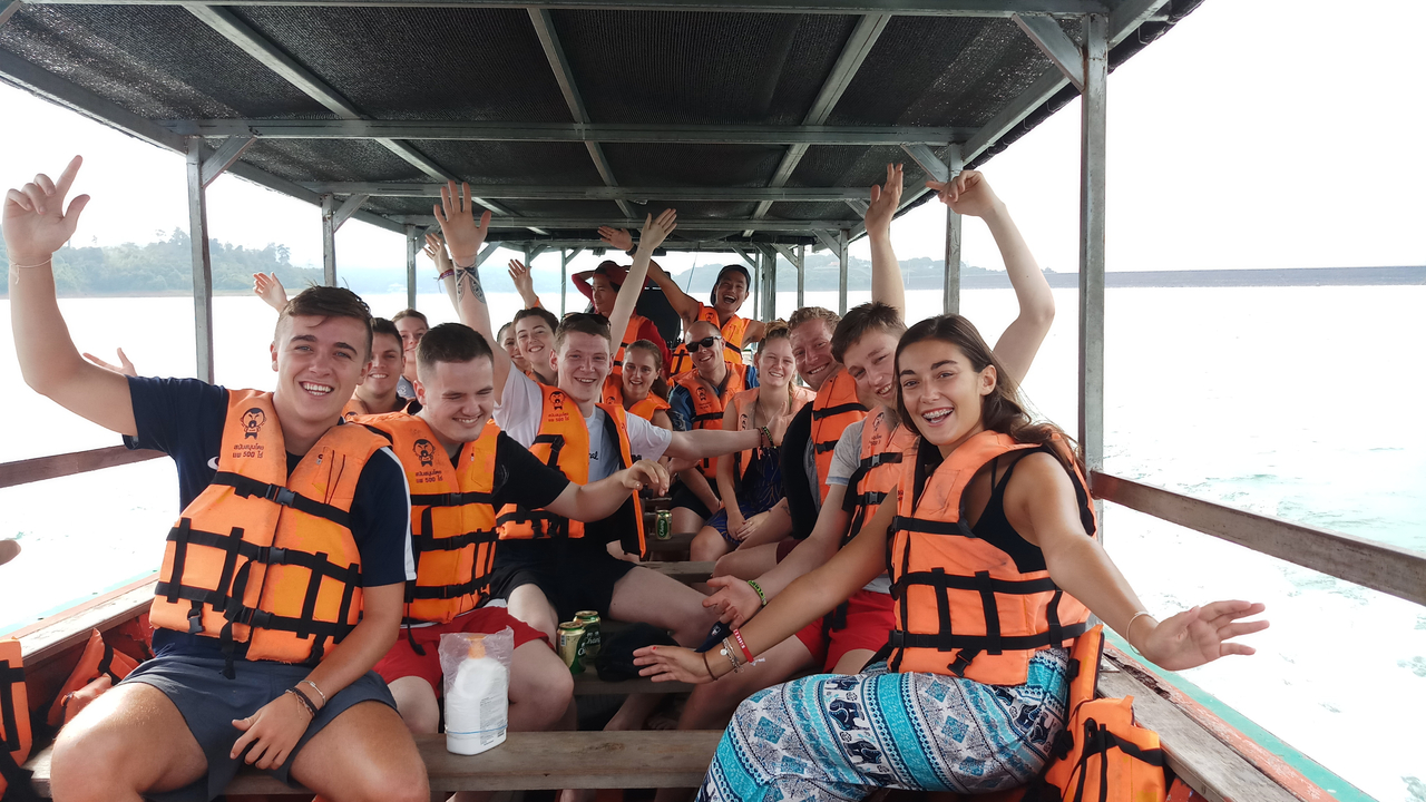 Group on a boat ride wearing life jackets, waving at the camera.