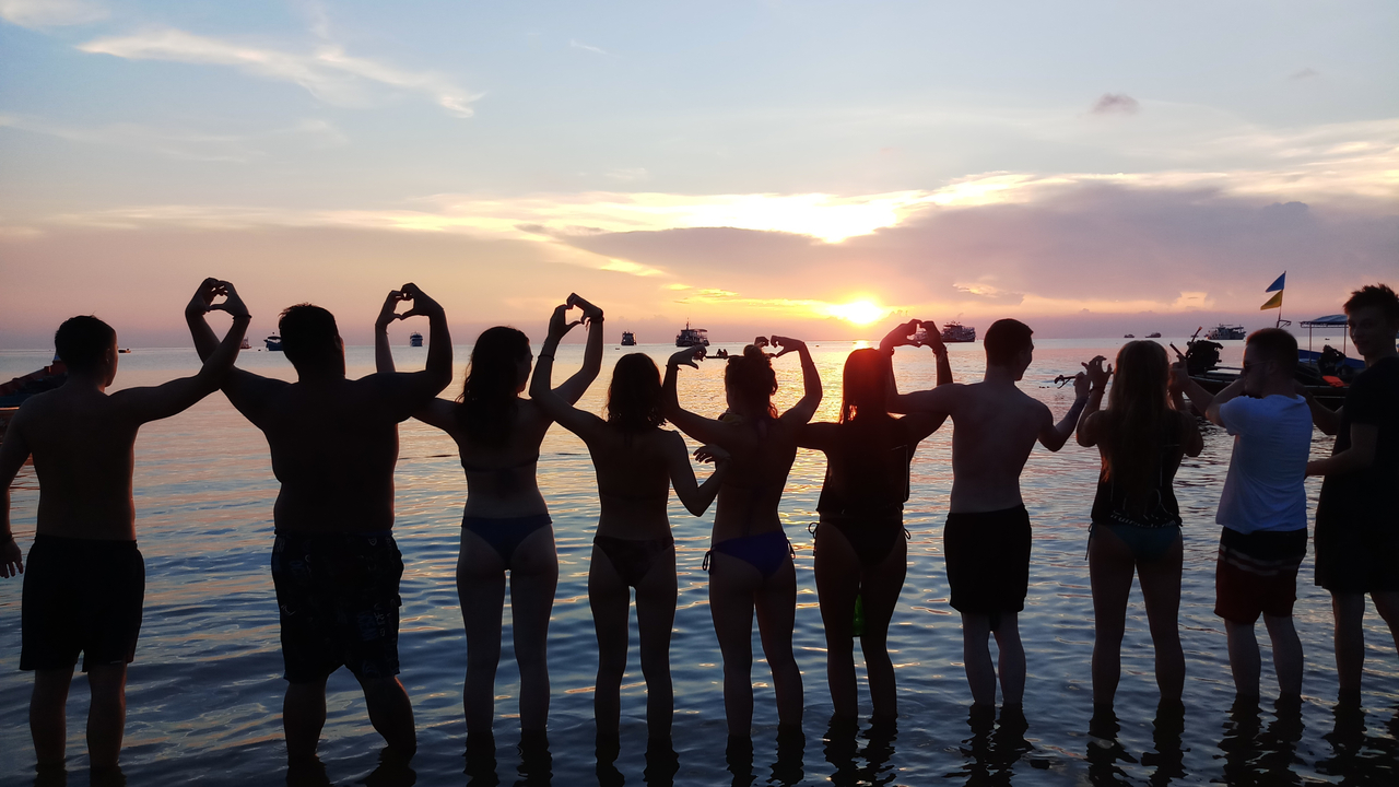 Silhouetted group in the sea making heart shapes at sunset.