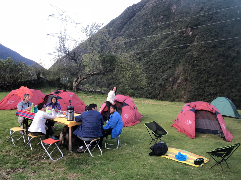 Scène de camping avec des personnes autour d'une table dans une région montagneuse.