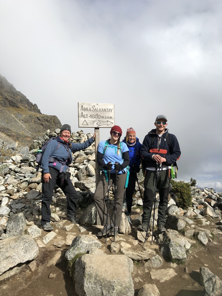 Groupe de randonneurs à un col d'altitude avec un panneau indicateur.